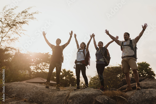 Backpacker group of four Asian men and women Standing at the top of the mountain  raising your hands in joy and success.