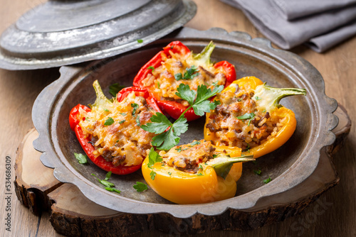Stuffed peppers, halves of peppers stuffed with rice, dried tomatoes, herbs and cheese in a baking dish on a blue wooden table, top view. Vegetarian dish, stuffed vegetables