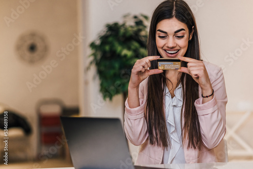 Surprised young adult businesswoman, admiring her credit card.