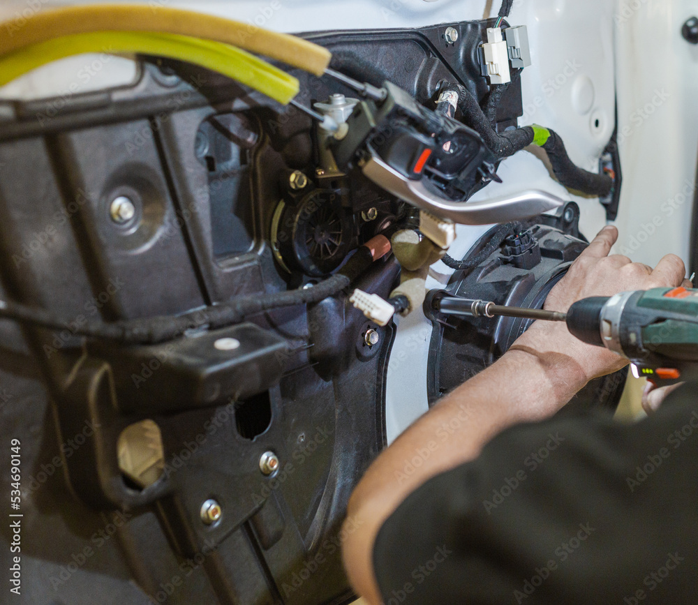 A car repairman repairs a car door. An auto mechanic works with the car door. A man works at a service station. A car repairman repairs a car door. An auto mechanic works with the car door. A man works at a service station.