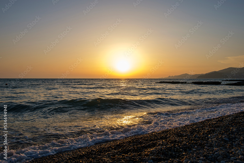Gorgeous sea sunset landscape. MIrror reflection of dawn on wet pebble. Golden sunlight over sea waves.