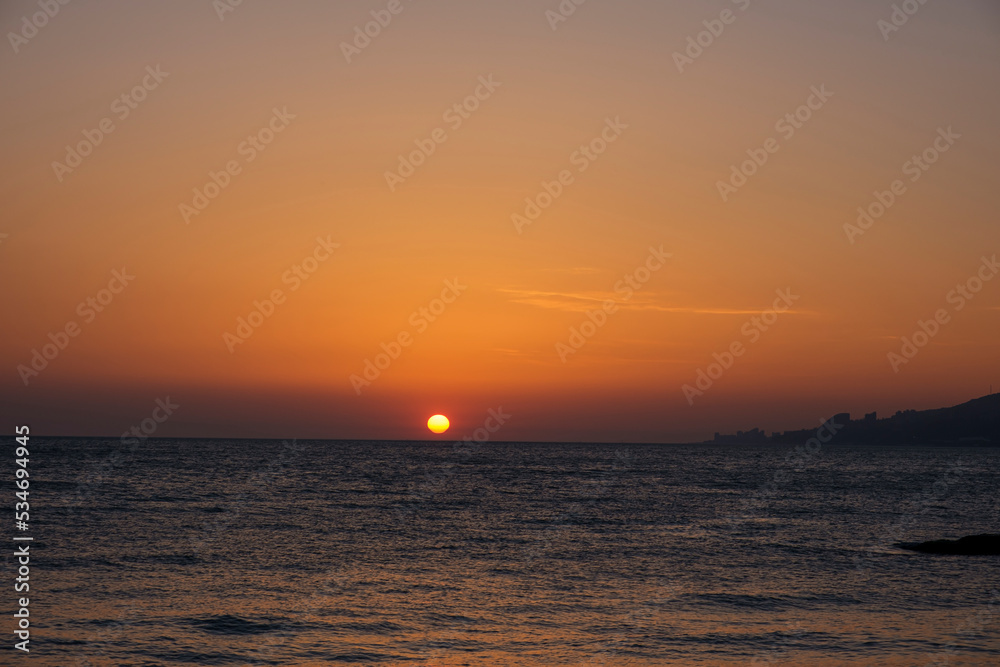 Fototapeta premium Gorgeous sea sunset landscape. MIrror reflection of dawn on sea surface. Red sun on cloudless sky, apocalypse. Blurred, out of focus