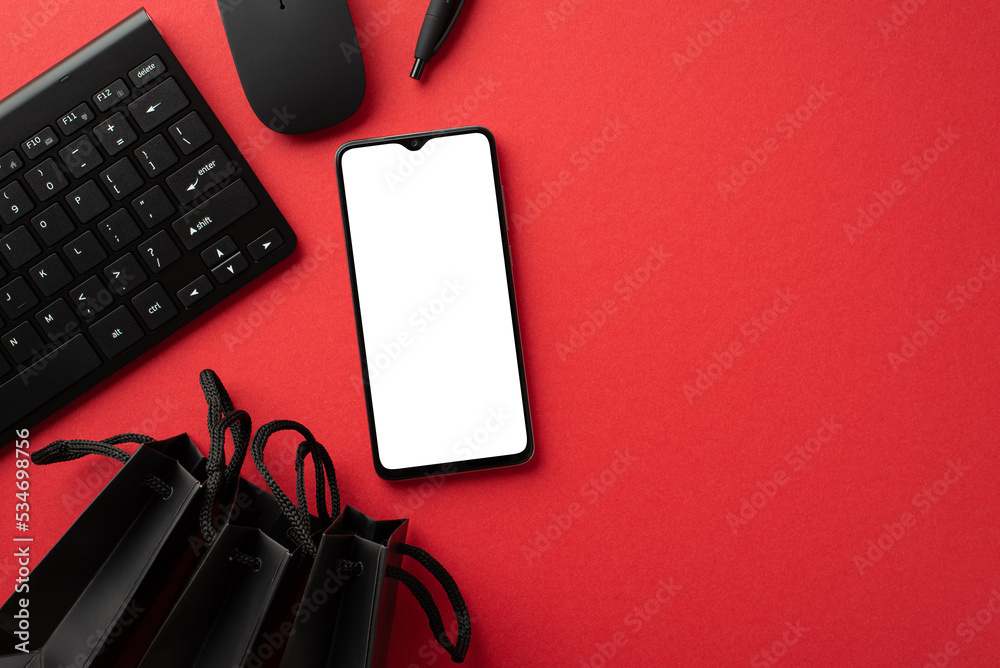 Black friday concept. Top view photo of smartphone black paper bags pen computer mouse and keyboard on isolated red background with empty space Black friday concept. Top view photo of smartphone black paper bags pen computer mouse and keyboard on isolated red background with empty space