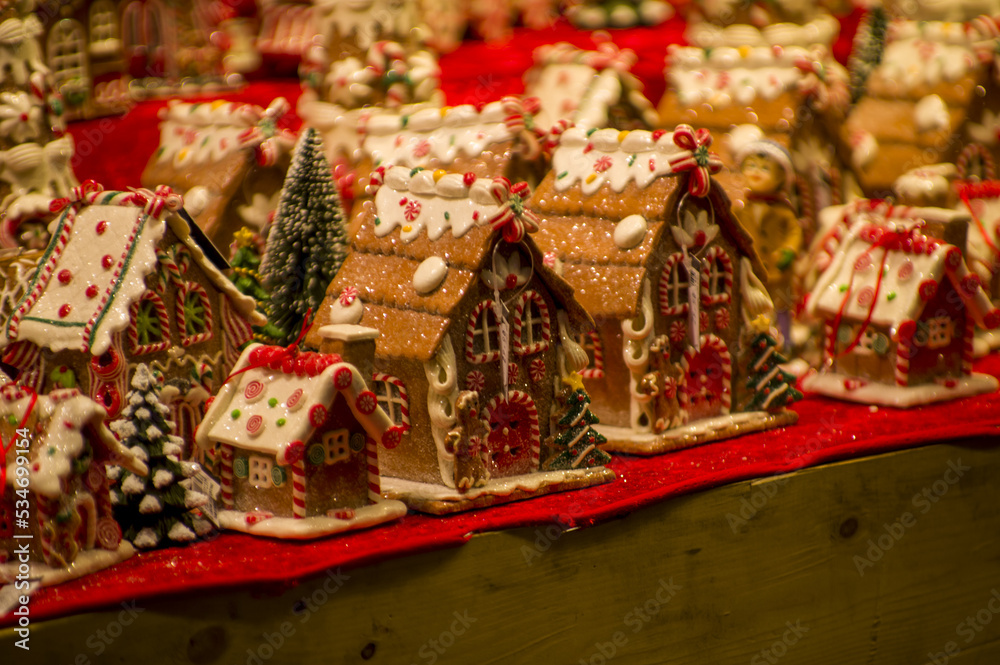 Fototapeta premium Advent Bazaar Stalls with glass, wooden, ceramic christmas souvenirs in a shop. Close up of festive decorations for tree in winter street night market during new year's holiday. Illuminated fair kiosk