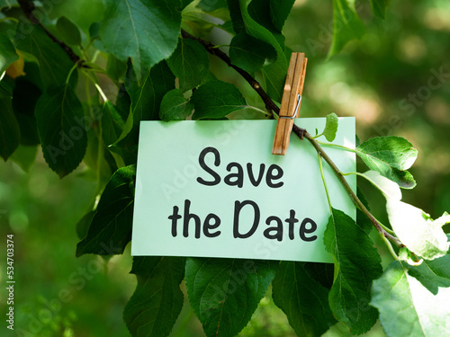 A green paper note with words Save the Date hanging on a tree branch © rosinka79