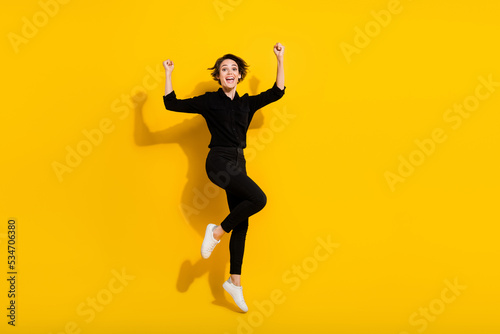 Photo of charming lucky girl dressed formal shirt jumping high rising fists empty space isolated yellow color background © deagreez