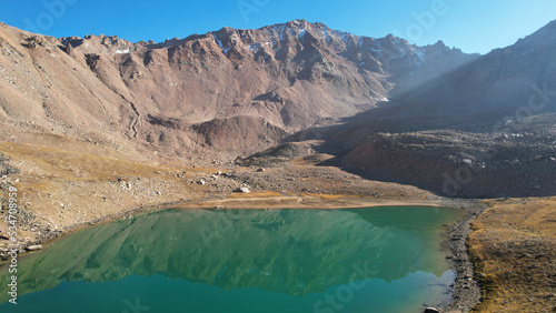 The emerald color of the water of a mountain lake. Drone view of a green mountain lake with a reflection of the mountains. Smooth transparent water. There are large stones nearby. Dry grass Kazakhstan