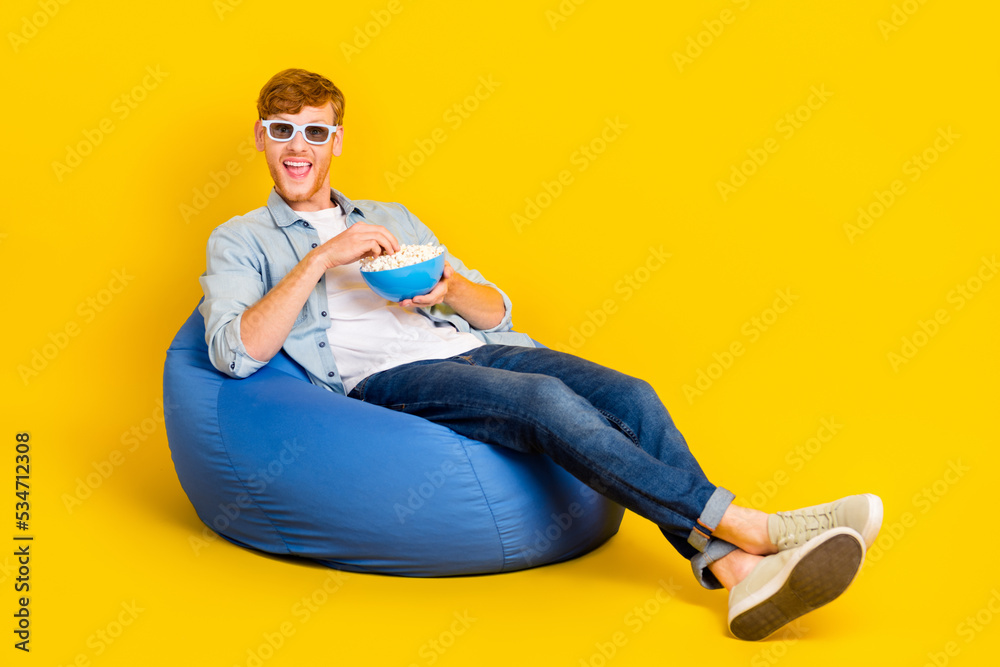 Photo of attractive impressed man wear jeans shirt vr eyewear sitting beanbag eating pop-corn empty space isolated yellow color background Photo of attractive impressed man wear jeans shirt vr eyewear sitting beanbag eating pop-corn empty space isolated yellow color background