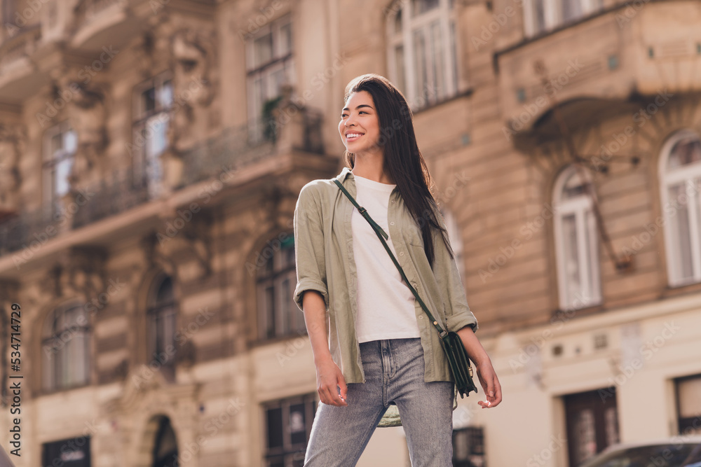 Photo of positive shiny young asian woman wear khaki shirt enjoying summer sunshine walking outside urban city street Photo of positive shiny young asian woman wear khaki shirt enjoying summer sunshine walking outside urban city street