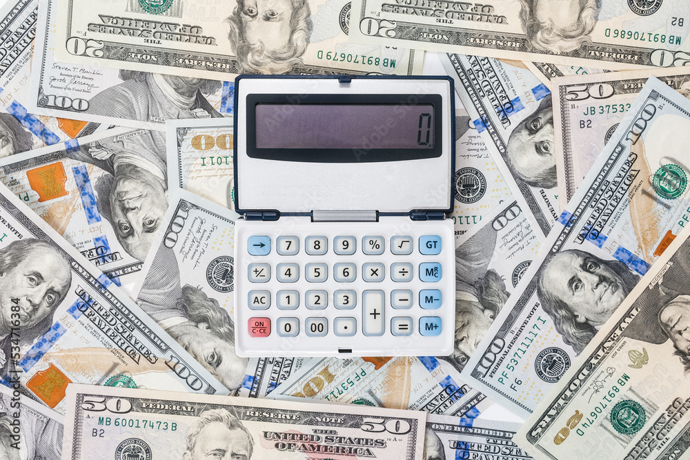 Finance and mortgage. Calculator is located on scattered new dollar bills, close-up. Flat lay. The concept of accounting, business and taxes