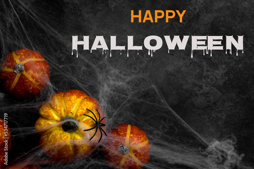 Happy Halloween written on background with pumpkins covered in spiderweb and spider on top. Top view,flat lay