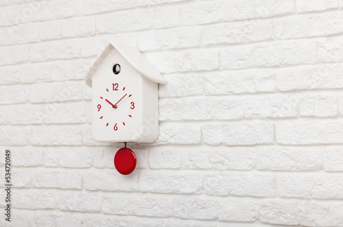 White cuckoo bird clock with red round pendulum and dial on a white brick wall with copy space