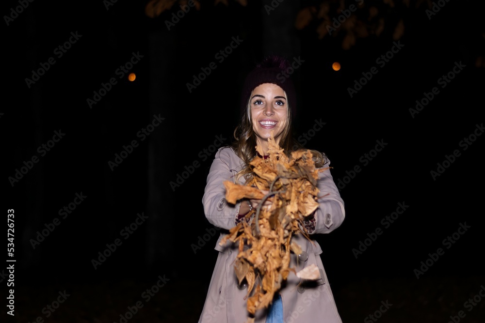 portrait of happy smiling caucasian woman throwing leaves at night in autumn