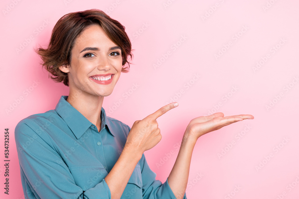 Photo portrait of adorable young lady toothy smile palm point empty space promo dressed trendy blue look isolated on pink color background Photo portrait of adorable young lady toothy smile palm point empty space promo dressed trendy blue look isolated on pink color background