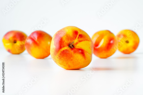 Ripe nectarine in center on white, several nectarines lined up behind it in a blur, space for text at top and bottom of photo, close-up, at eye level