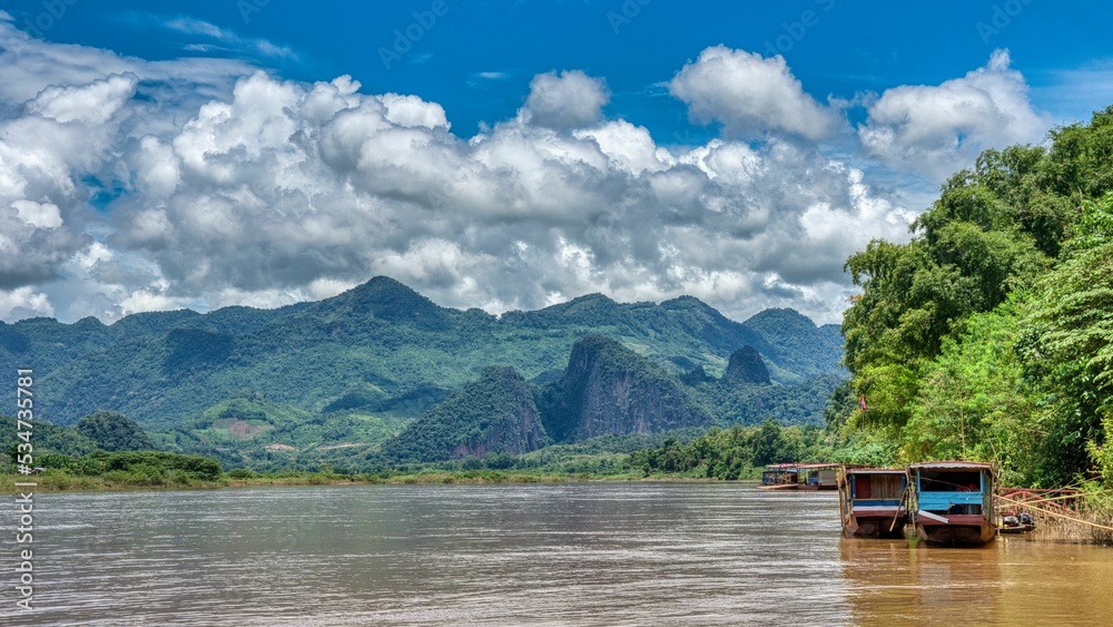 Mekong River at Luang Prabang, lang boats are parked at the shore, beatiful river beetwen mountain forest, cloudy sky, high quality photo