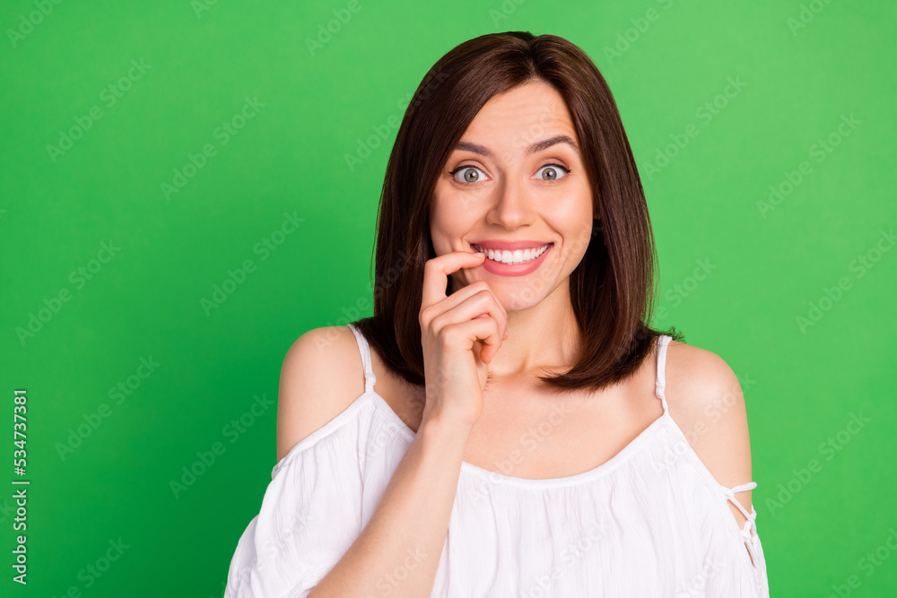 Photo portrait of stunning young woman excited bite nail beaming smile dressed trendy white clothes isolated on green color background Photo portrait of stunning young woman excited bite nail beaming smile dressed trendy white clothes isolated on green color background