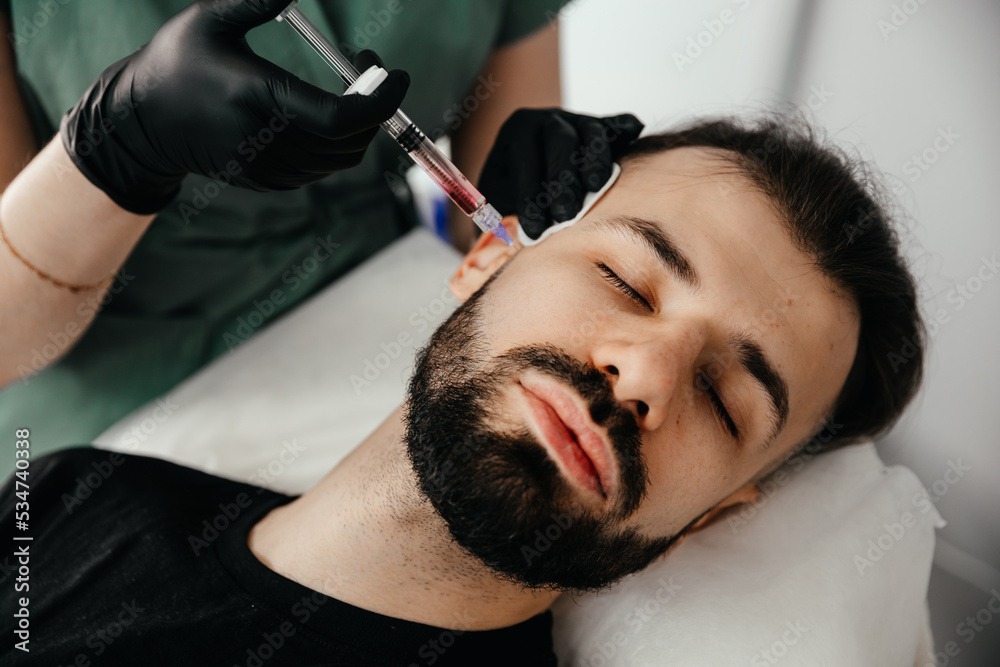 Fototapeta premium Beauty treatments for a stylish young man with a beard. Beautician makes beauty injections in a man's face