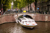 barco de turistas pasando bajo un arco de un puente en un canal en amsterdam, holanda, países bajos