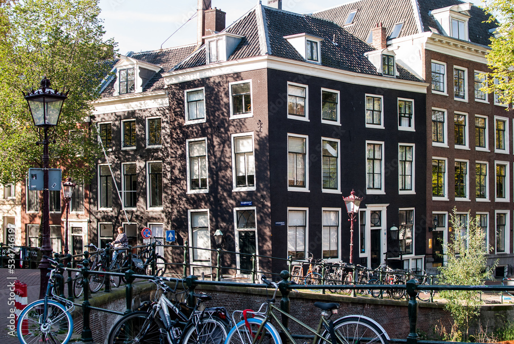 Edificio, haciendo esquina, de ladrillos negros marcos de ventanas blancos con bicicletas y farola en primer plano junto a un canal en amsterdam, países bajos, holanda