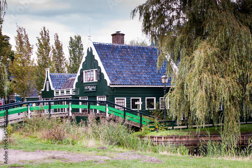 casas tradicionales en un vecindario rural verdes con tejas negras y un puente de acceso sobre un canal en el pueblo De Zaanse Schans en holanda, países bajos