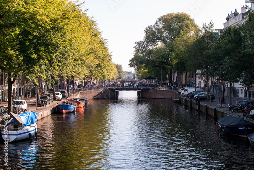 canal con agua y embarcaciones y árboles a los lados y puente al fondo en amsterdam, países bajos, holanda