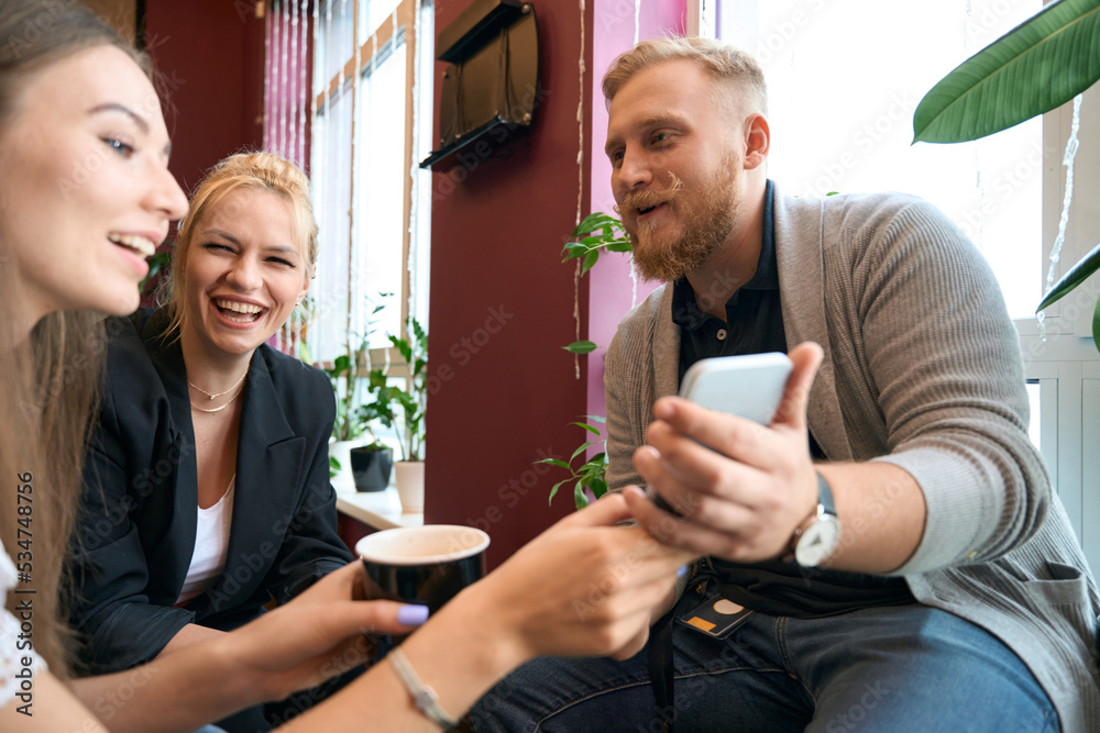 Male demonstrating photos on smartphone to ladies during coffee break