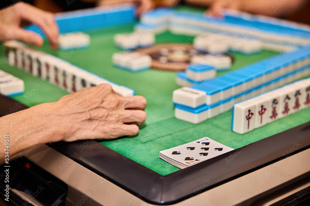 Fototapeta premium Elderly people playing mahjong, indoor gamble activity at home during spring festival.