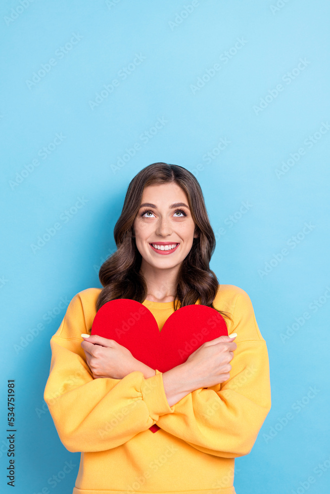 Vertical closeup photo of young adorable toothy woman wear pullover positive hold red paper heart hug pretty look empty space isolated on blue color background Vertical closeup photo of young adorable toothy woman wear pullover positive hold red paper heart hug pretty look empty space isolated on blue color background