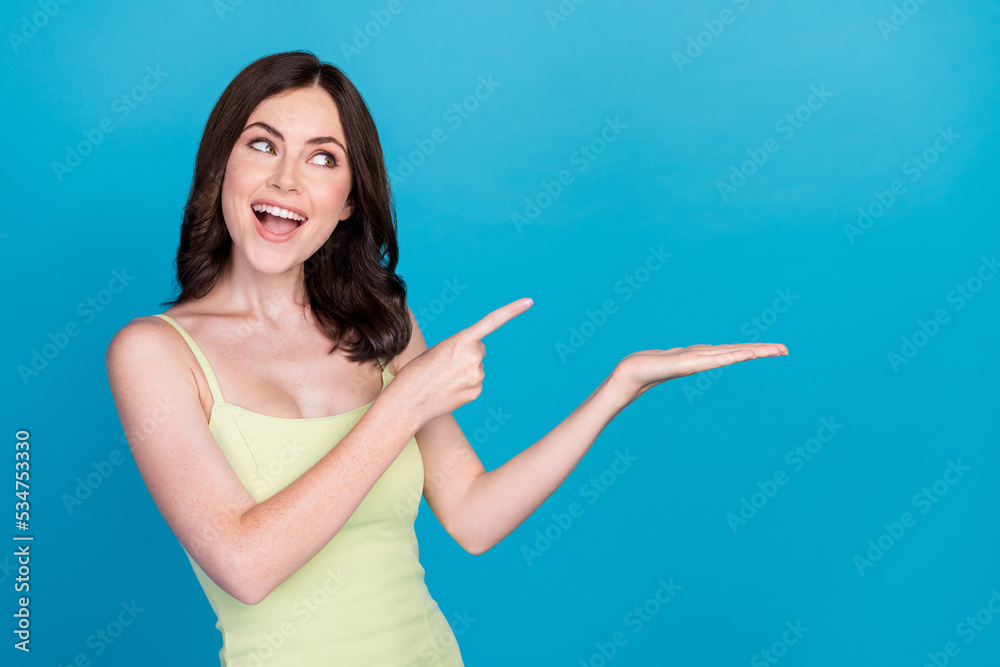 Photo of funny cheerful girl look indicate finger hand hold empty space isolated on blue color background Photo of funny cheerful girl look indicate finger hand hold empty space isolated on blue color background