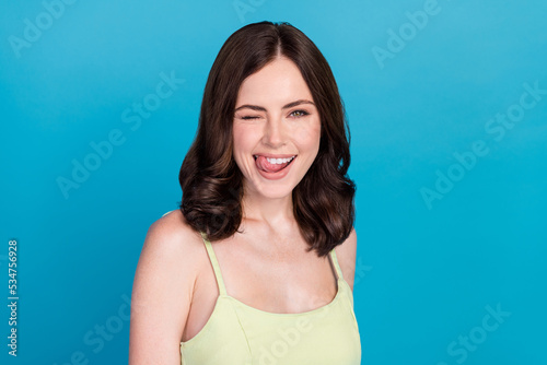 Photo of sweet tricky girl dressed green dress licking lips winking smiling isolated blue color background