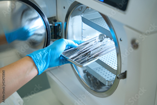 Woman hand in gloves puts dental instrument into sterilization apparatus