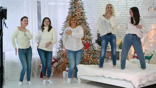 Five adult female girlfriends have fun and dance macarena against the backdrop of a Christmas tree and decor in the room. photo