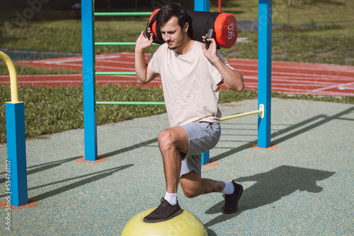 ambitious athlete is preparing for the competition season. A man with a 10kg dumbbell with water on his shoulders does a lunge on a balance beam. Training coordination and smaller muscle groups photo