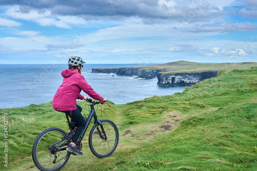 nice senior woman on mountain bike, cycling on the cliffs of Dunmore Head near Kilballyowen , County Limerick in the southwestern part of the Republik of Ireland