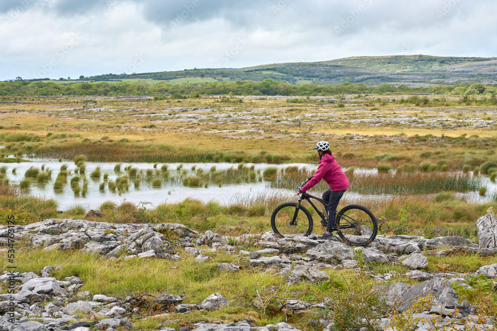 Obraz premium nice senior woman on mountain bike, cycling in the rough karst landscape of Burren near Ballyvaughan, County Clare in the western part of the Republic of Ireland