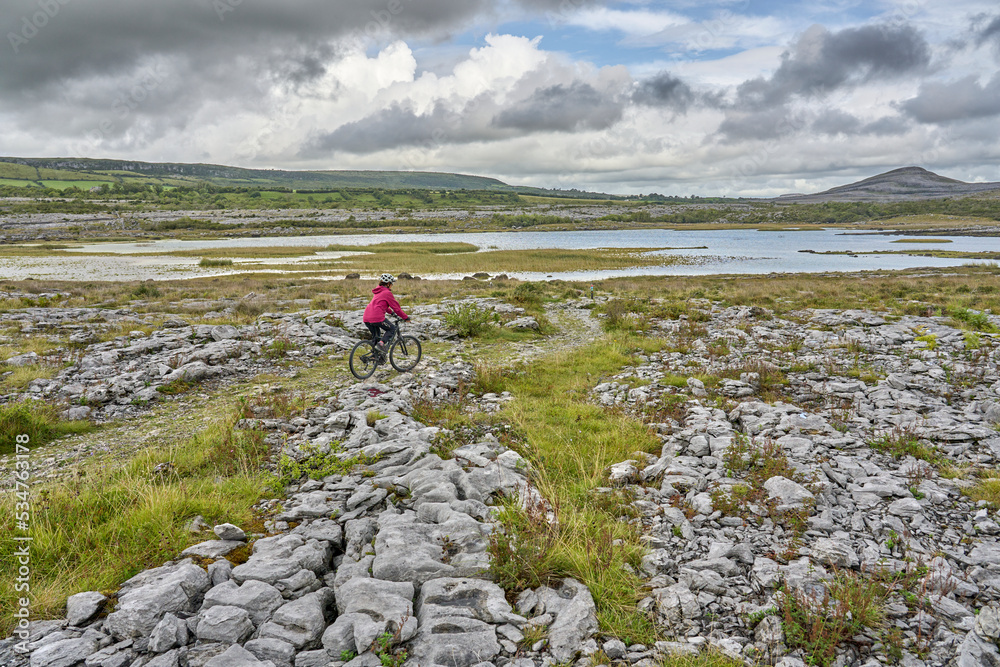nice senior woman on mountain bike, cycling in the rough karst landscape of Burren near Ballyvaughan, County Clare in the western part of the Republic of Ireland