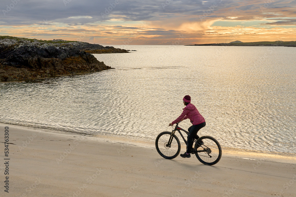 Fototapeta premium nice senior woman on mountain bike, cycling in sunset at the golden sand beach of Sillerna, Grallagh, County Galway, in the western part of the Republic of Ireland