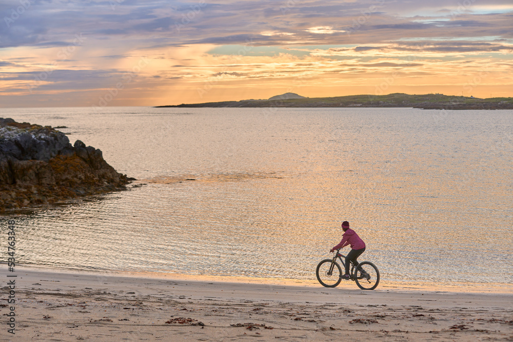 Fototapeta premium nice senior woman on mountain bike, cycling in sunset at the golden sand beach of Sillerna, Grallagh, County Galway, in the western part of the Republic of Ireland