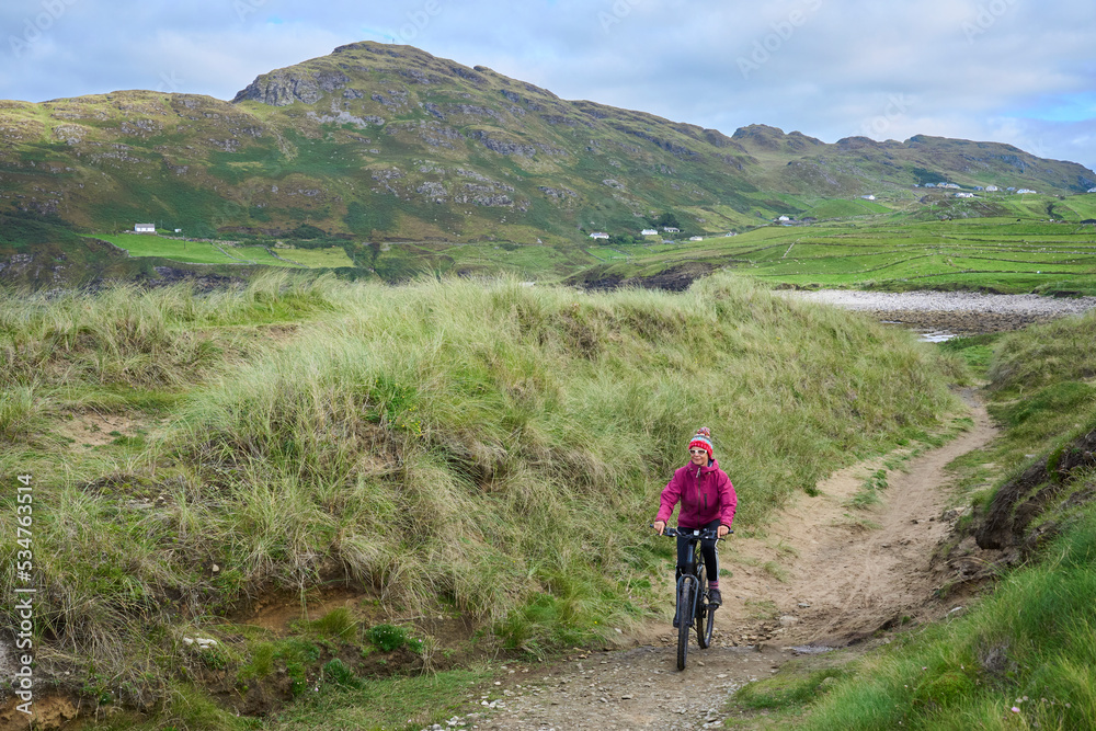 nice senior woman carrying her  mountain bike, on the cliffs of Malin Head, Donegal, the northern most point of Ireland