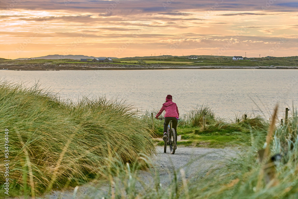 nice senior woman on mountain bike, cycling in sunset in the sand dunes of Sillerna, Grallagh, County Galway, in the western part of the Republic of Ireland