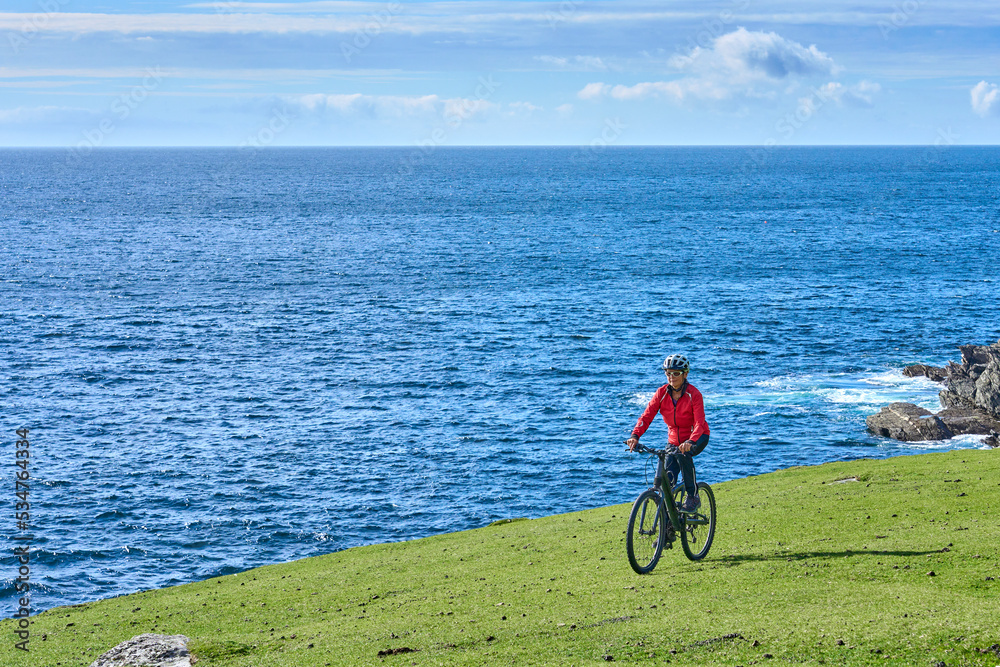 Fototapeta premium nice senior woman on mountain bike, cycling on the cliffs of Achill Island, Carrowgarve, Republik of Ireland
