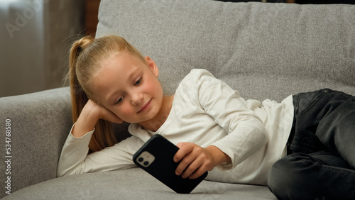 Billede på lærred Smart kid user of young generation junior girl use modern smartphone rest on sof