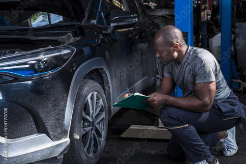 Black african mechanic man holding clipboard check lists car problem in auto repair shop, Car Maintenance Concept