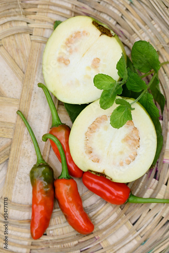 closeup the bunch ripe yellow white guava fruit sliced with red chilly and green leaf in the brown basket soft focus natural white brown background.