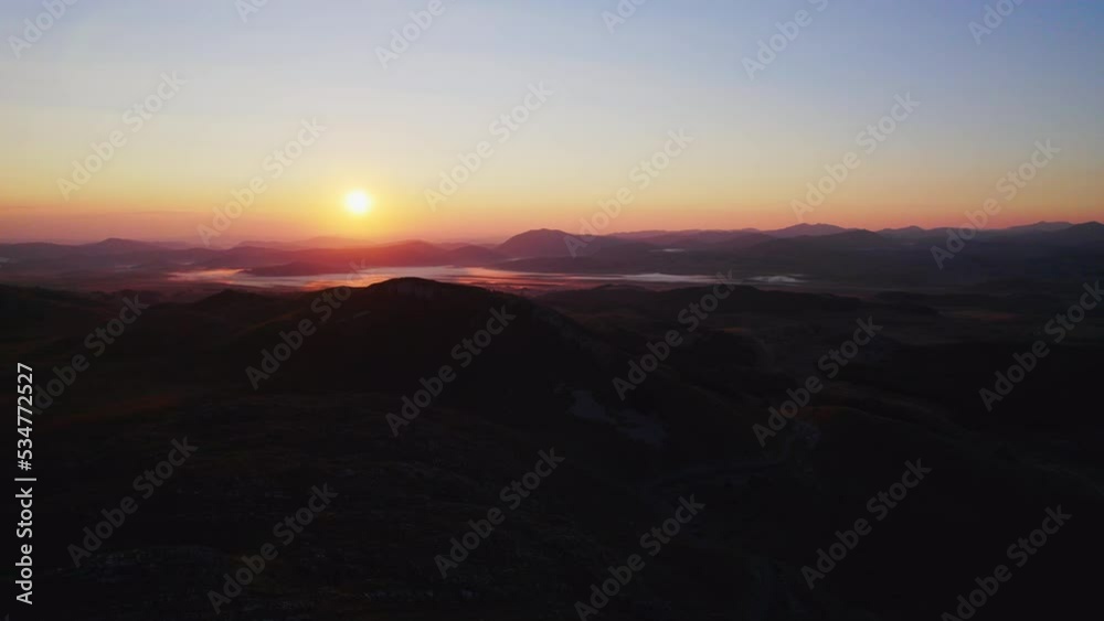 Aerial shot at dawn from the mountaintops towards the valley showing low fog and the rising sun, the drone moves forwards, edited with minimal color correction Aerial shot at dawn from the mountaintops towards the valley showing low fog and the rising sun, the drone moves forwards, edited with minimal color correction