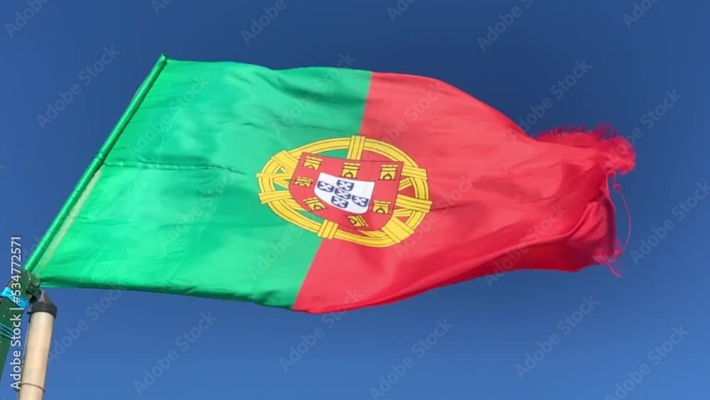 Waving flag of Portugal in windy weather with blue sky in the background. Slow motion