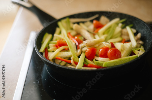 Cooking in the kitchen at home in a pan of fresh vegetables cut into strips: cherry tomato, zucchini, red pepper, eggplant