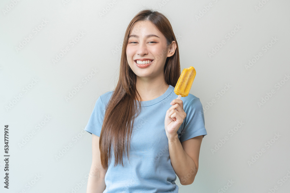 Cheerful enjoy, happy cute asian woman wearing casual with brunette hair, eating popsicle, teenage girl holding ice pop, lolly frozen stick with mango yellow, passion fruit ice cream tasty in summer. Cheerful enjoy, happy cute asian woman wearing casual with brunette hair, eating popsicle, teenage girl holding ice pop, lolly frozen stick with mango yellow, passion fruit ice cream tasty in summer.