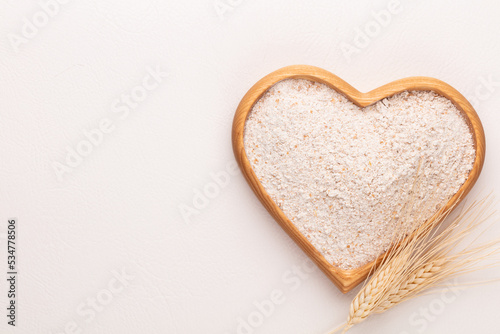 Wheat flour in a wooden heart shape bowl on a pastel background.